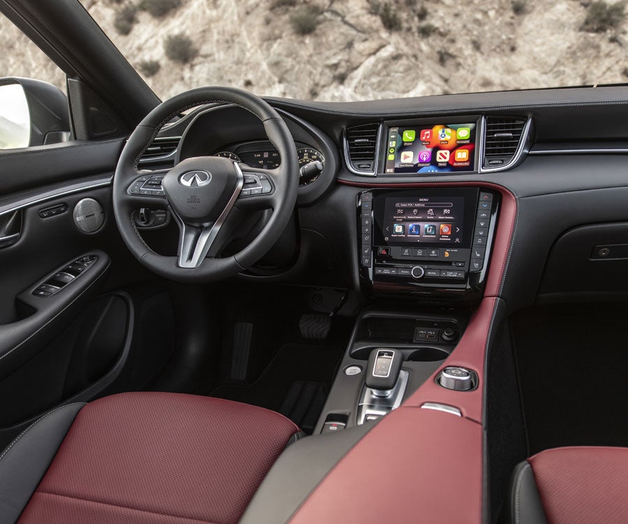 Interior of an Infiniti QX50 car with a black dashboard, two display screens, and a red and black leather seat.