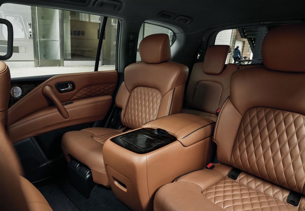Brown leather interior of a car Infiniti QX80 , showing two rows of quilted seats and a center console with a glossy black lid.