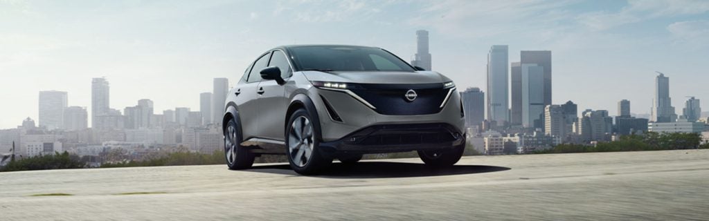 Gray Nissan Ariya electric SUV with a city skyline background.
