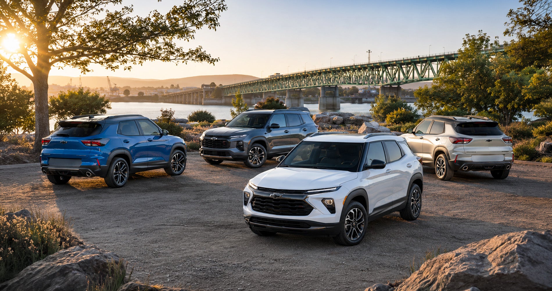 Four Trailblazer SUVs in blue, white, gray, and beige parked near waterfront bridge at sunset, showcasing full trim range.