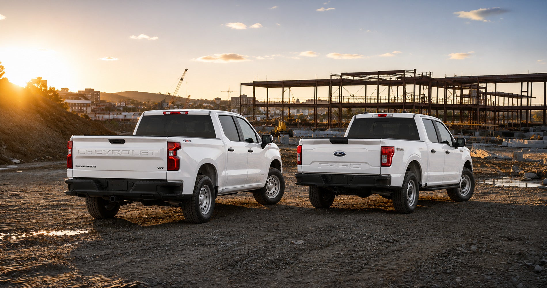 Rear view of white Chevrolet Silverado WT and Ford F-150 XL at a construction site during sunset, highlighting work-ready design.