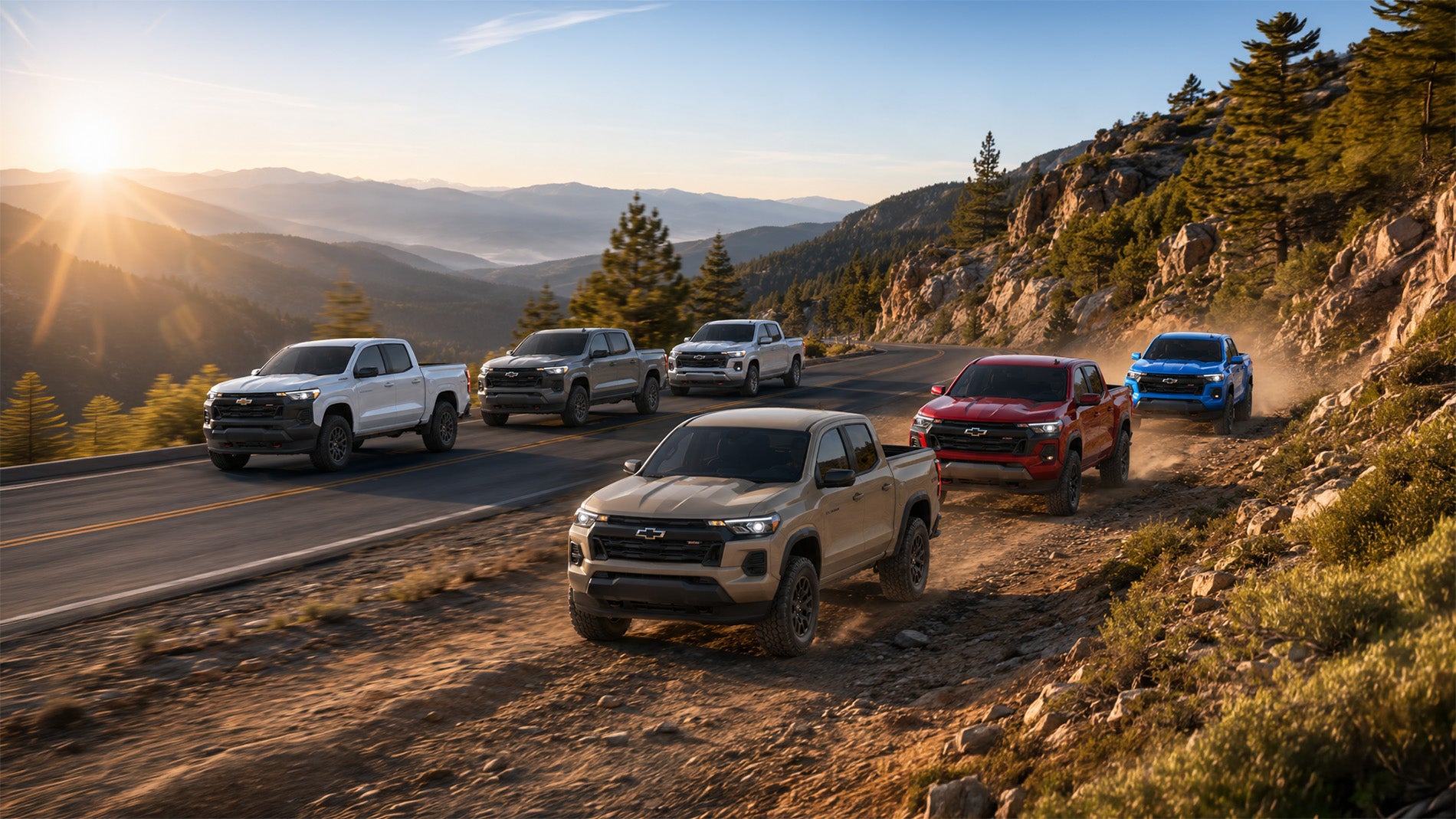 Six 2026 Chevrolet Colorado pickup trucks in tan, white, gray, red, and blue drive along a mountain road and adjacent trail at sunrise, showcasing the range of Colorado trim levels available at Delta Chevrolet in Pittsburg, CA.