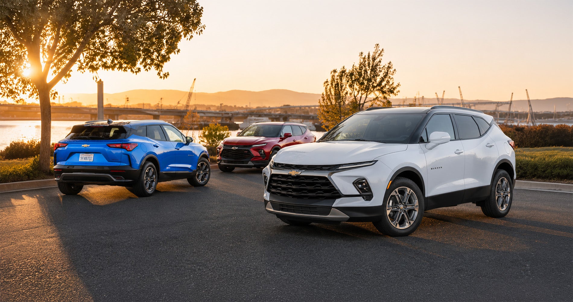 Blue, red, and white Blazer SUVs parked near waterfront bridge at sunset, showcasing full trim range.
