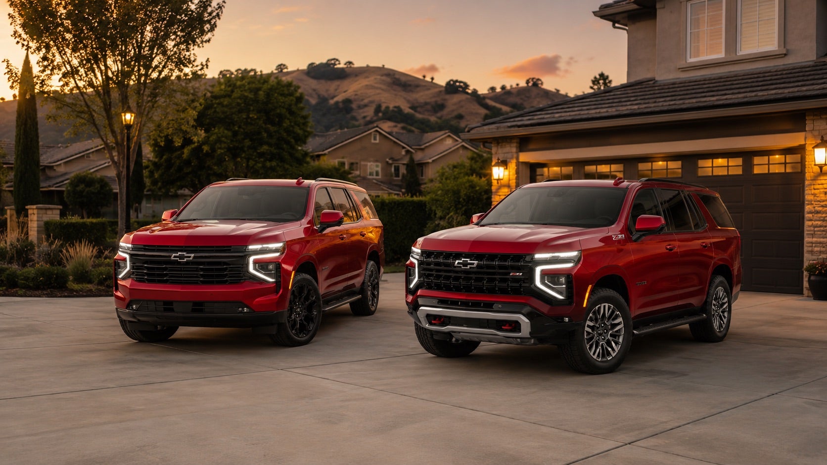 Two red 2026 Chevrolet Tahoe SUVs parked side by side in a residential driveway at sunset, showcasing distinct front‑end designs for sport‑styled and off‑road Z71 trims available at Delta Chevrolet in Pittsburg, CA.