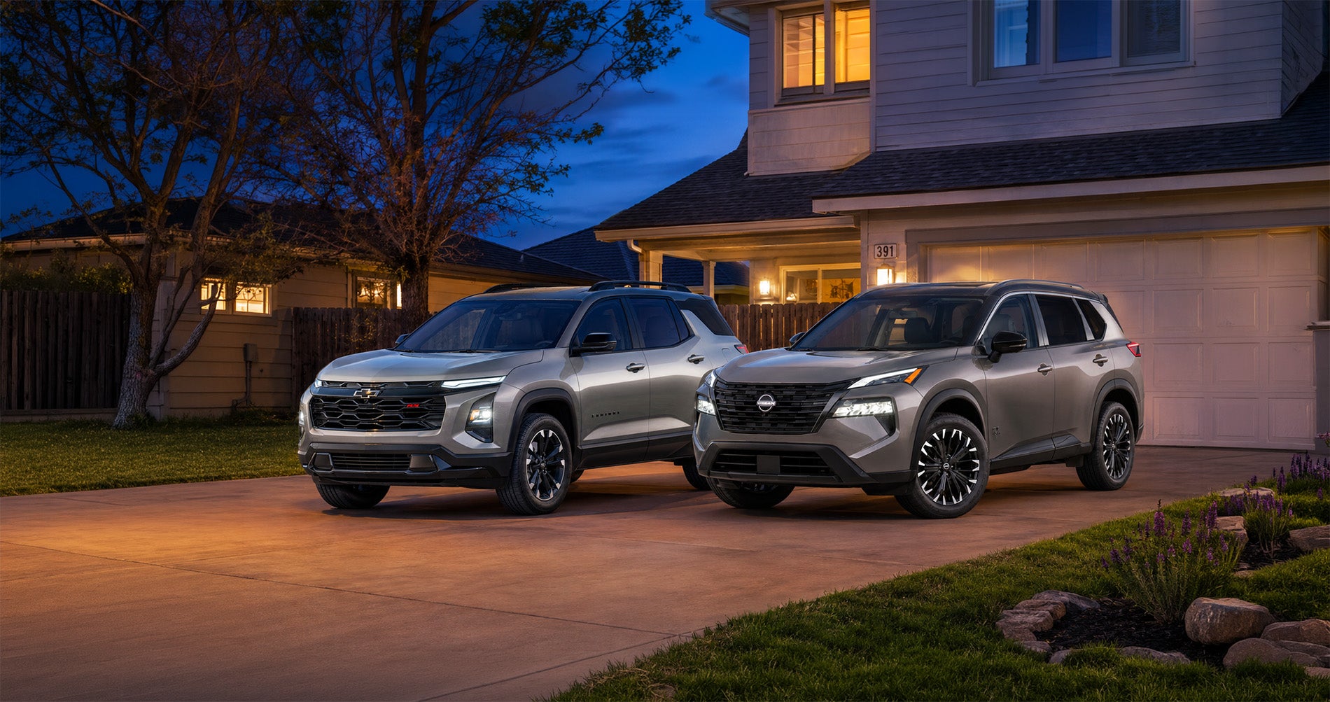 Two silver SUVs—a 2027 Chevrolet Equinox and a 2026.5 Nissan Rogue—parked side by side in a residential driveway at dusk in Pittsburg, California, with warm house lights and a tree in the background, highlighting their modern styling and design differences.