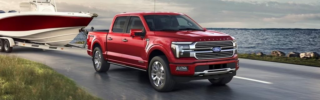 Red Ford F-150 truck towing a boat on a trailer next to a lake