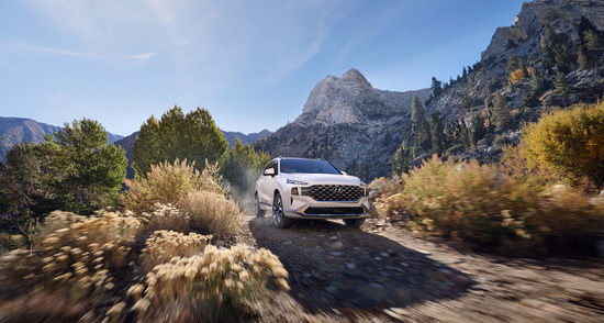 A Hyundai Santa Fe SUV on a dirt road, with a family hiking ahead in a mountainous landscape.