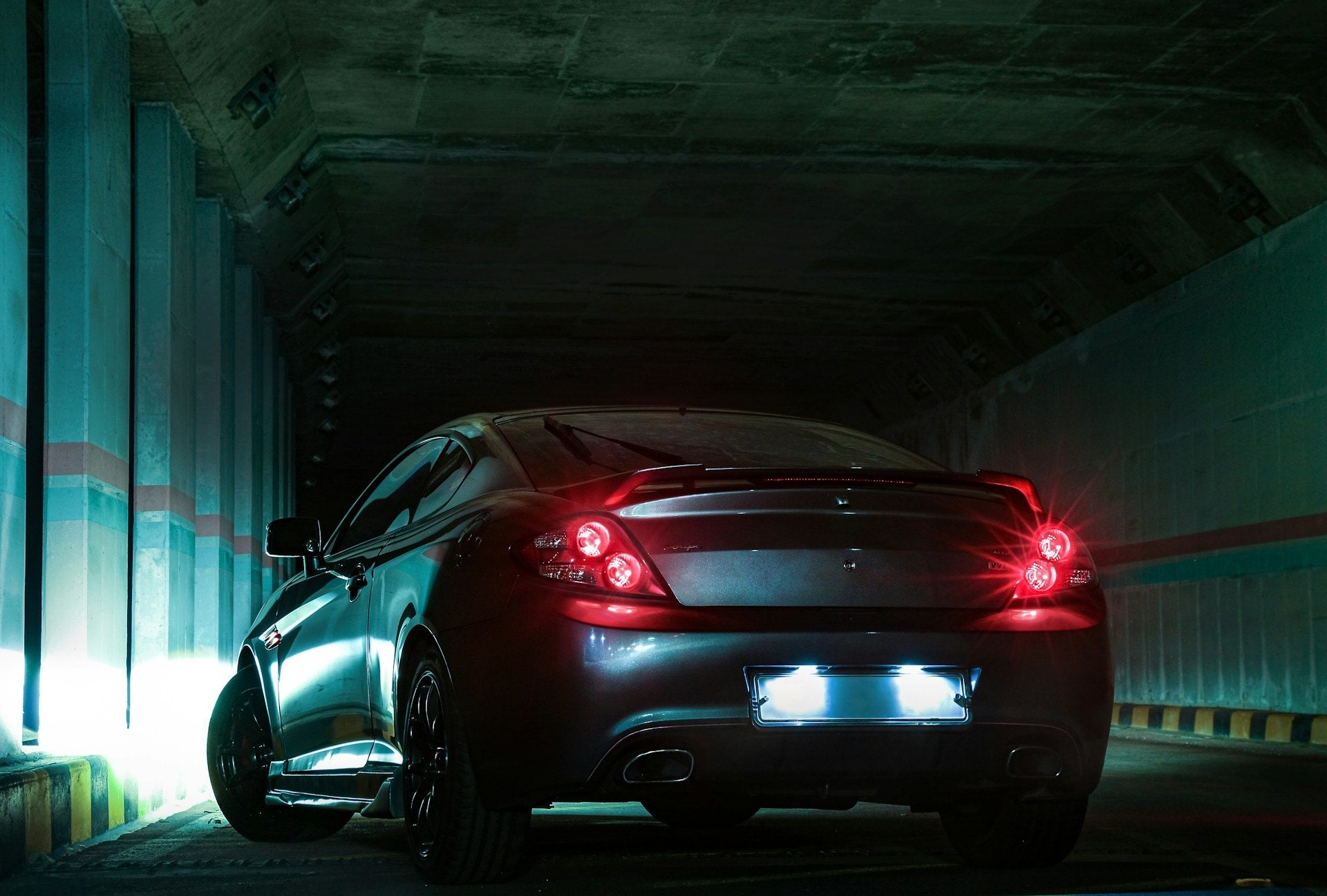 Rear view of a dark blue Hyundai Tucson driving down a city street at night, with buildings and streelights blurring in the background.