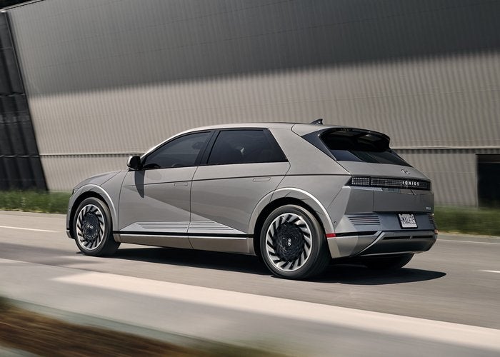 A gray Hyundai Ioniq 5 electric car parked on a paved road next to a modern building.