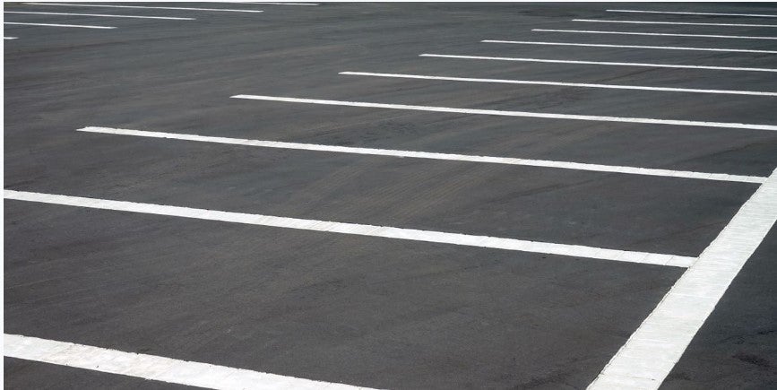 Empty paved parking lot with white painted space lines marking parking spots.