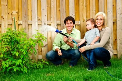 family watering plants beside wooden fence around a house