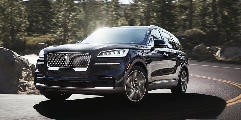 A black Lincoln Aviator driving on a winding road through a forest