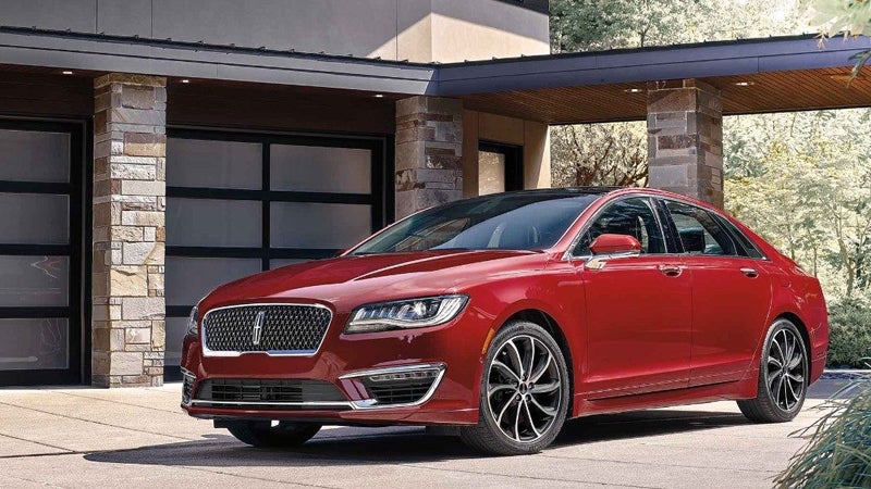 Red Lincoln MKZ sedan parked outside a modern house with stone pillars.
