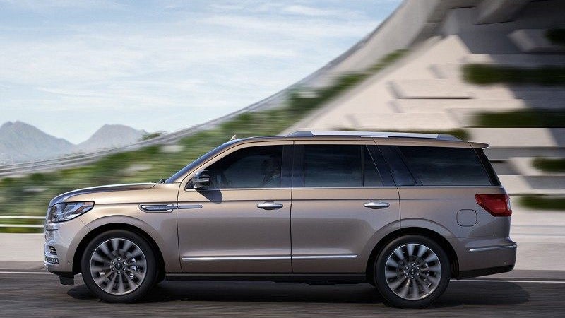 Profile view of a bronze luxury SUV driving on a highway.