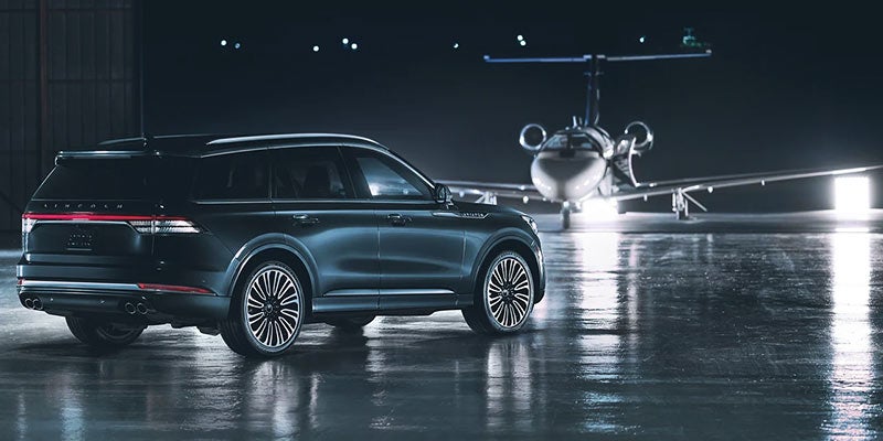 A dark Lincoln SUV parked in a hangar next to a jet