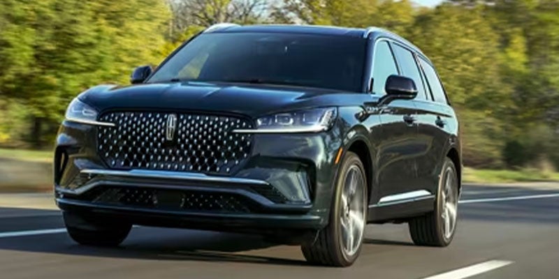 Dark green Lincoln Corsair SUV driving through a dense, foggy evergreen forest.