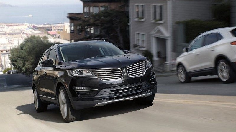 Black Lincoln MKZ driving on a city street past residential buildings