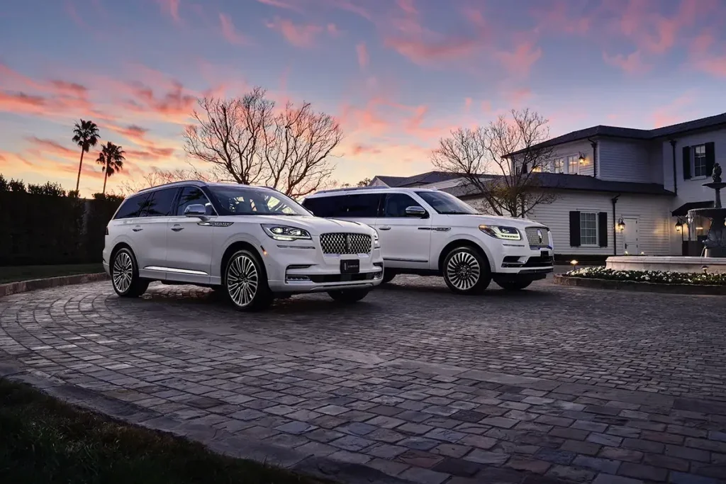Two white Lincoln SUVs parked before a building with white siding