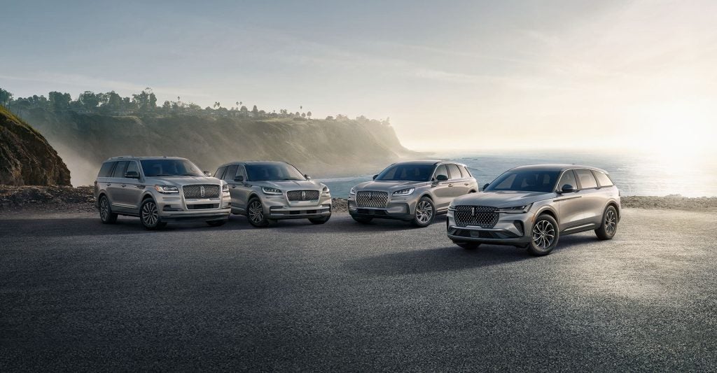 Four silver Lincoln SUVs parked on a cliffside overlooking the ocean