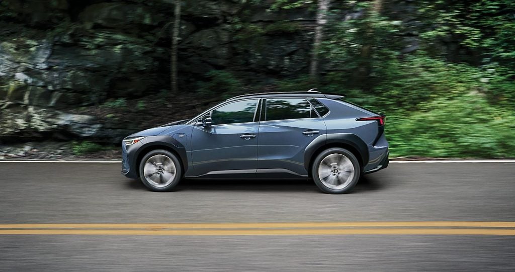Side profile of a EV Subaru SUV driving on a road with a forested background.
