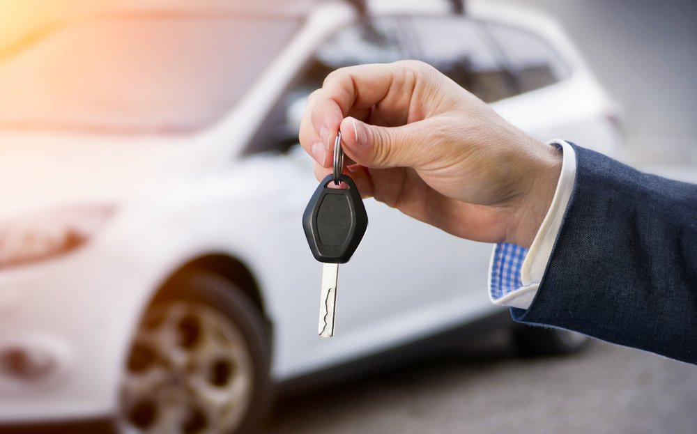 A well-dressed person in a suit and tie extending their hand to offer car keys.