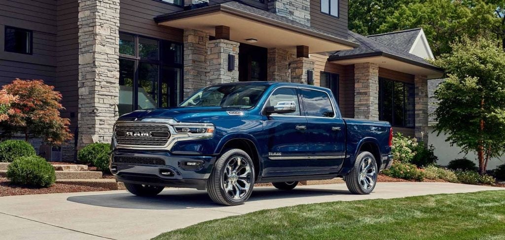 A blue Ram 1500 truck with chrome wheels is parked on a driveway in front of a stone and wood house.