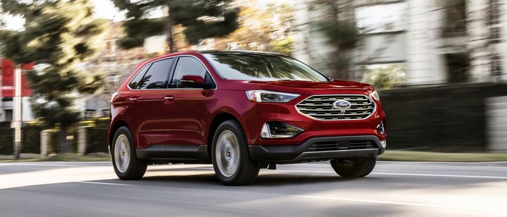 Red Ford Edge SUV driving on a city street, motion blur indicating speed.