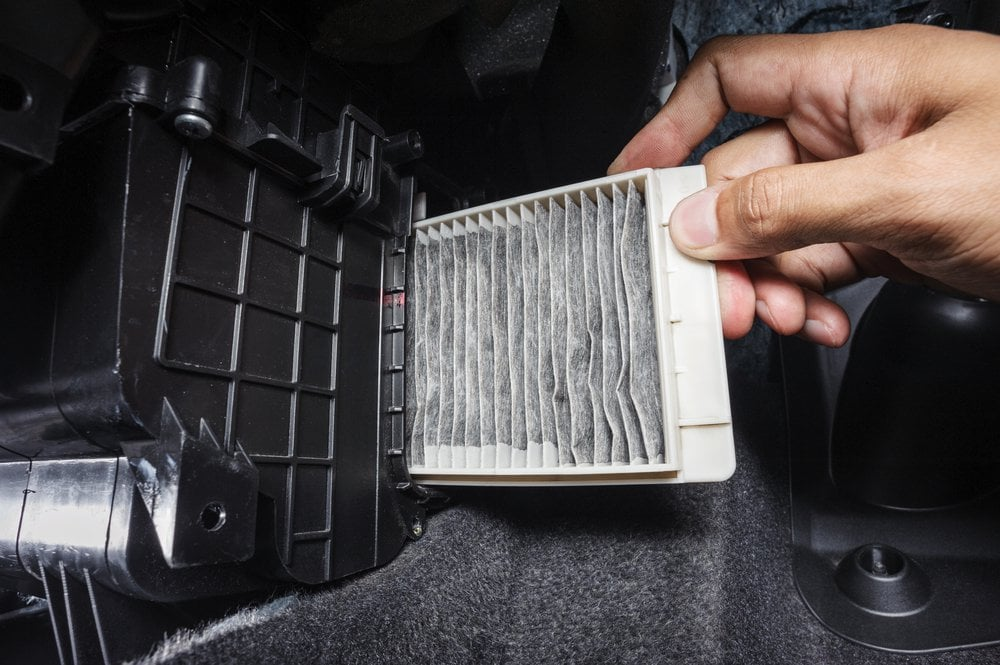 A mechanic installing a new white air filter into a black car engine compartment.