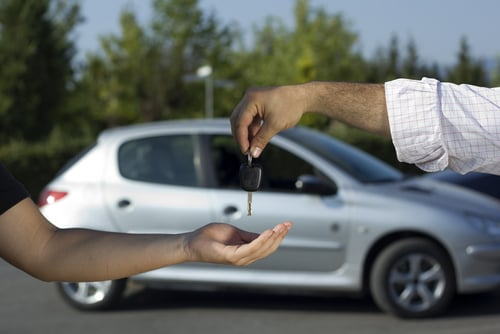Two people exchanging car keys for a thick stack of cash, likely a car deal.
