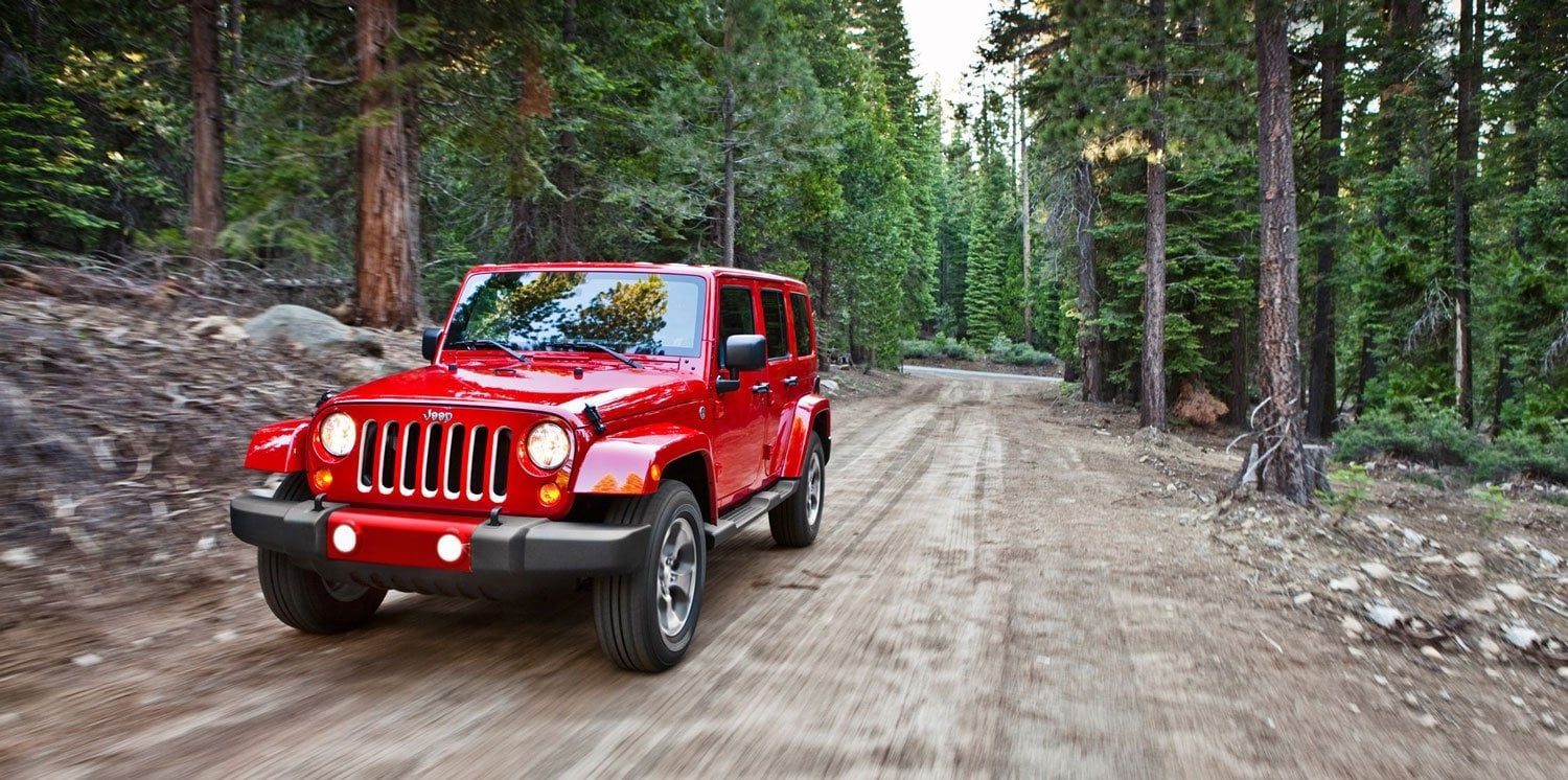 REd 4-door Jeep Wrangler on a winding mountain road with autumn trees and a metal guardrail.