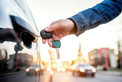 Person holding a modern car key and remote entry fob, ready to unlock a car.