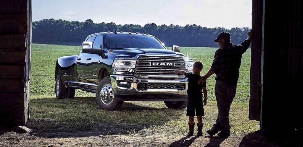 A dark blue Ram 3500 pickup truck with a father and son looking at it from an open barn door, facing a green field.
