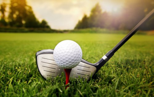 A golf ball on a tee with a golf club.