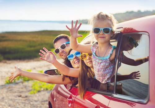 Family and dog admiring a bright orange sunset over hills and valleys from beside an open car trunk.