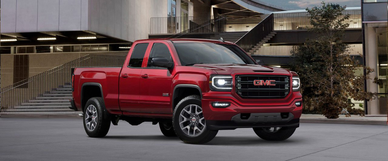 Red Ford F-150 Lightning electric pickup truck driving on a city street, buildings in background.