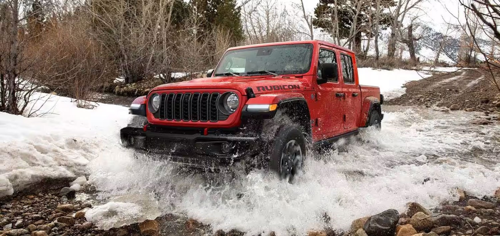A Red Jeep Gladiator pickup truck driving on a snowy road.