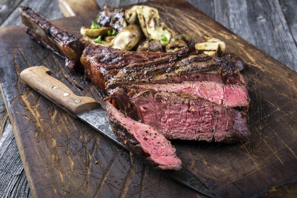Sliced medium-rare steak served on a wooden board with cherry tomatoes