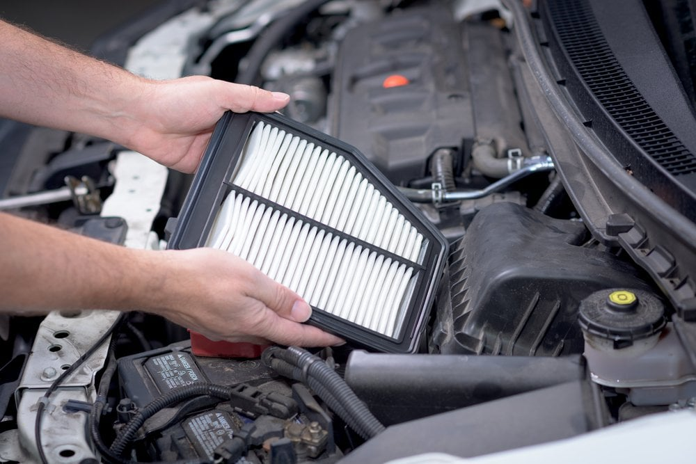 A mechanic wearing high-grip gloves inserts a new rectangular engine air filter into a car.