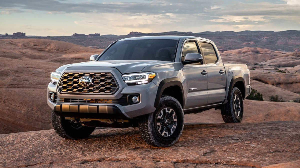 Grey Toyota Tacoma pickup truck kicking up dust while driving through a barren, mountainous desert landscape.