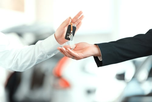 One person hands over car keys as another holds a stack of cash, suggesting a vehicle purchase or sale.