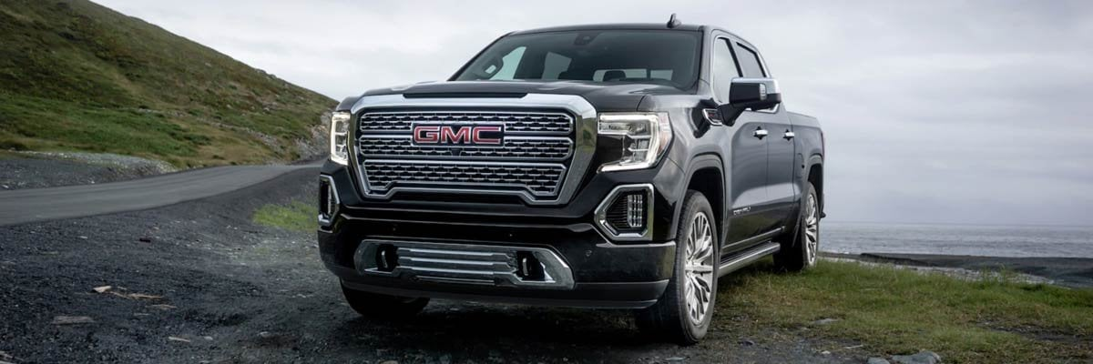 A black GMC pickup truck parked on a grassy hillside with in the background.
