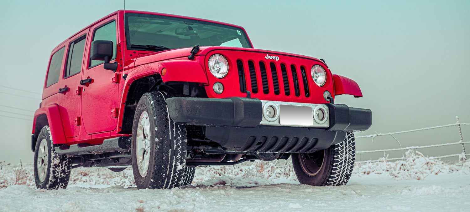 Red Jeep driving through a snowy stream.