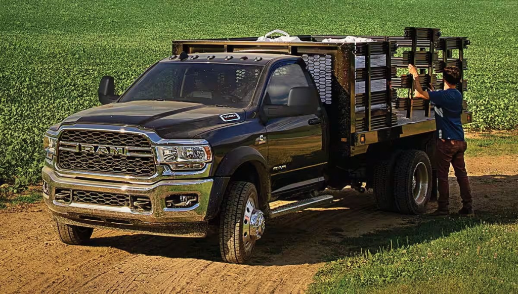 Front view of a Ram pickup truck driving down a rural dirt road with farming equipment visible in the background