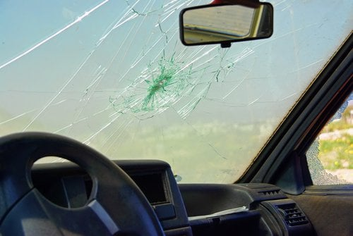 A shattered car windshield with a prominent star-shaped crack and radiating lines from a central impact point.
