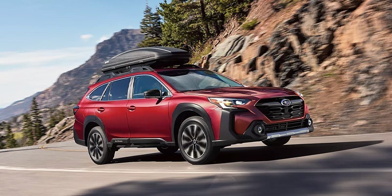 Red Subaru Outback driving on a mountain road with a rooftop cargo box.
