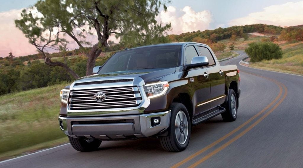 Dark brown Toyota Tundra pickup truck driving on a winding two-lane road through a hilly, green landscape.