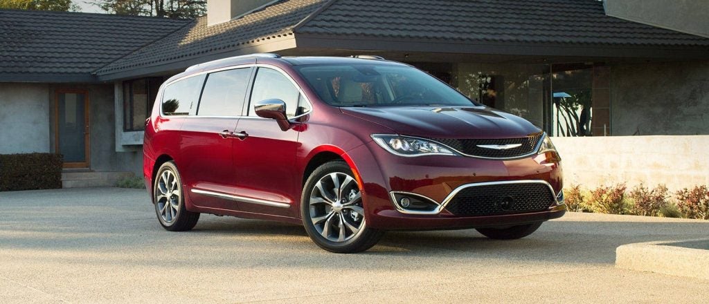 A dark red Chrysler Pacifica minivan parked on a driveway in front of a modern house on a sunny day.