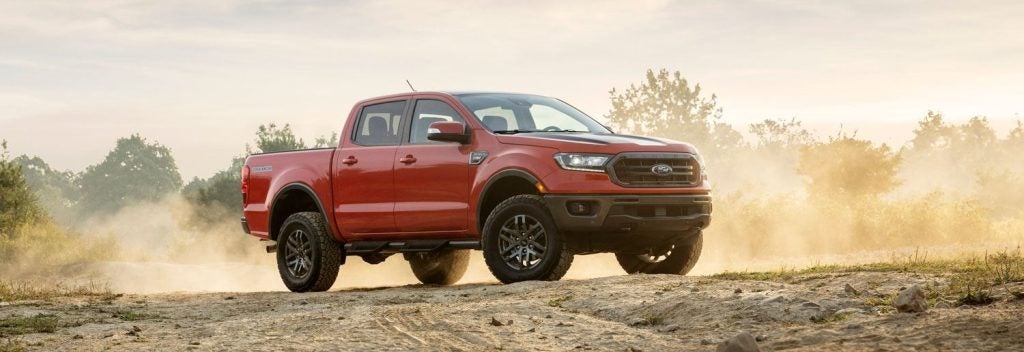 An orange Ford Ranger Tremor with black accents and off-road tires kicks up dust on a dirt road.