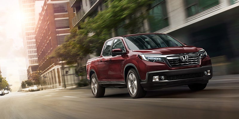 Maroon Honda Ridgeline pickup truck driving through a sunny city street
