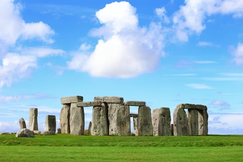 Stonehenge, a prehistoric circle of large standing stones, on a green grassy plain under a bright blue sky.